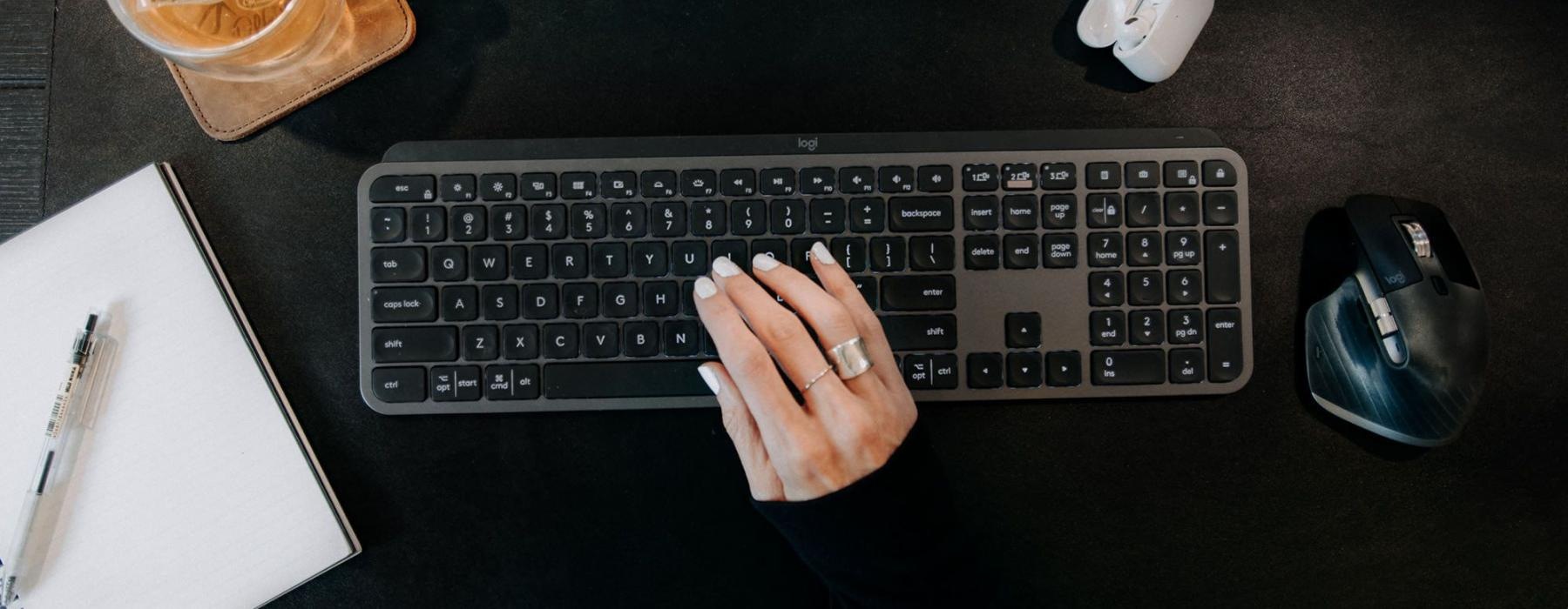 woman's hand on a keyboard surrounded by office items and a cup of tea on a coaster